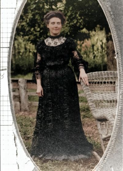 Restored and colorized (AI-assisted); faces are the original photo, colours are a best guess. Lucinda Bowles Peters, full-length portrait beside a wicker chair.