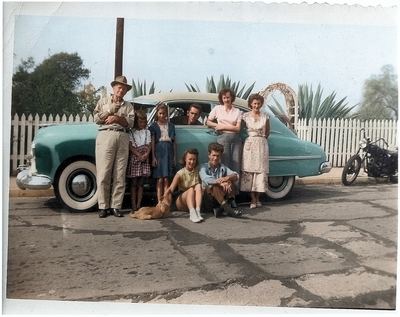 Restored and colorized (AI-assisted); faces are the original photo, colours are a best guess. Family group beside a car, captioned by the uploader "Proeger family c. 1950".